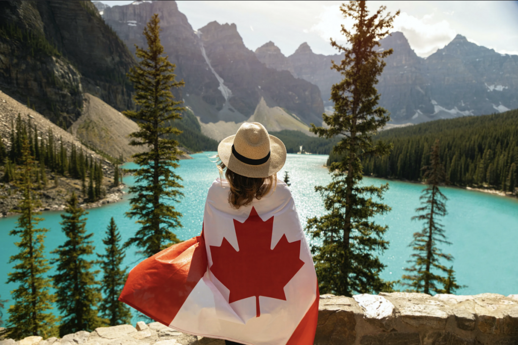 Mujer con bandera de Canadá frente al Lago Moraine en las Montañas Rocosas.