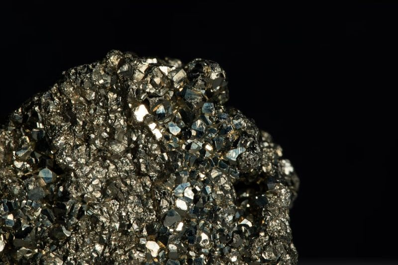 Primer plano de un mineral brillante con cristales metálicos dorados sobre un fondo negro.
