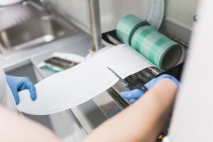 Profesional con guantes cortando material impreso en una máquina de impresión en un entorno industrial.
