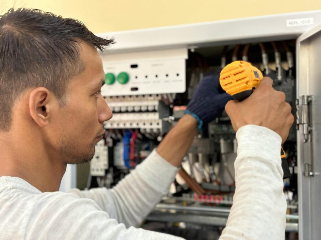 Electricista trabajando en un cuadro eléctrico utilizando un destornillador, revisando conexiones y cableado interno.