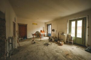 Estancia interior en proceso de reforma con suelo sin terminar, herramientas de obra, hormigonera y materiales de construcción distribuidos por la habitación.