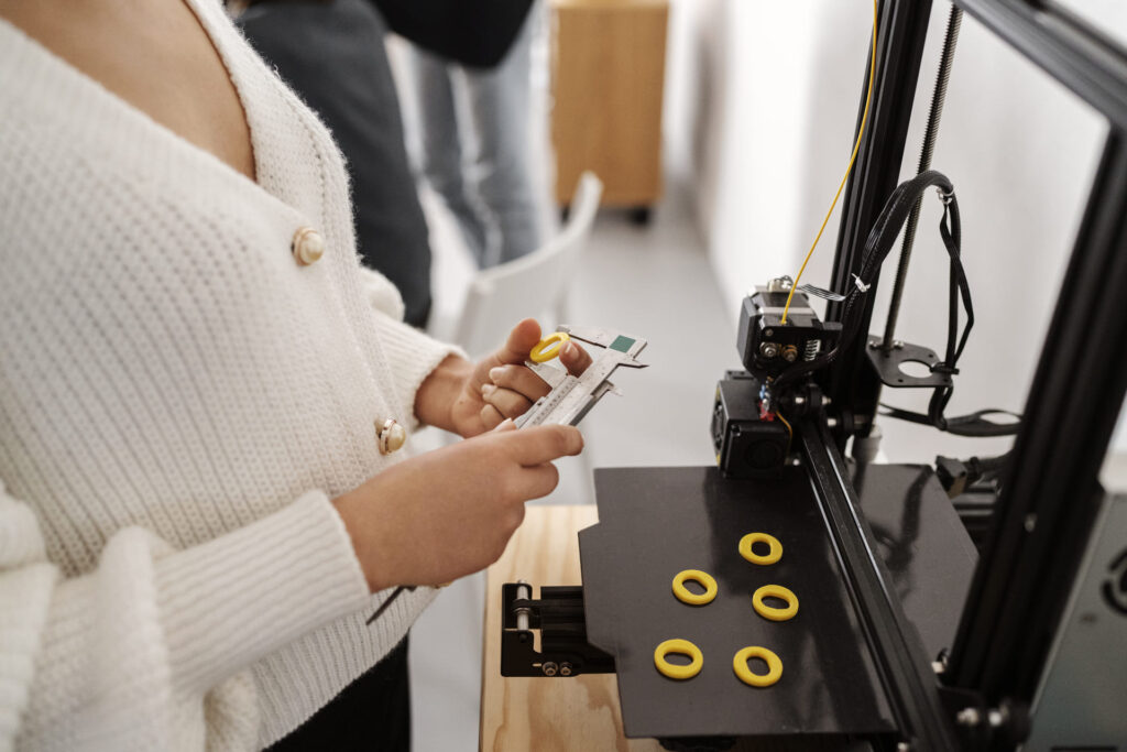 Persona midiendo piezas amarillas recién impresas en una impresora 3D con un calibre digital en un entorno de trabajo técnico.
