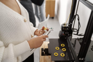 Persona midiendo piezas amarillas recién impresas en una impresora 3D con un calibre digital en un entorno de trabajo técnico.