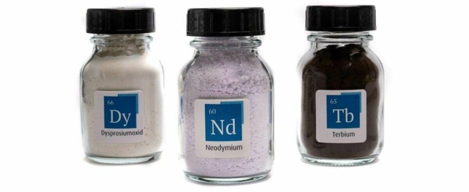 Frascos de laboratorio con muestras de tierras raras etiquetadas como disprosio, neodimio y terbio sobre fondo blanco.