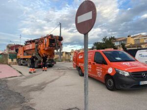 Operarios realizando trabajos de desatasco y limpieza de tuberías con camión cuba y vehículo de asistencia en una zona residencial.