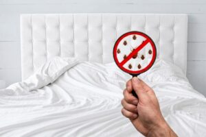 Cama con sábanas blancas y una lupa mostrando chinches tachadas con un símbolo de prohibición, representando la eliminación de una infestación de chinches