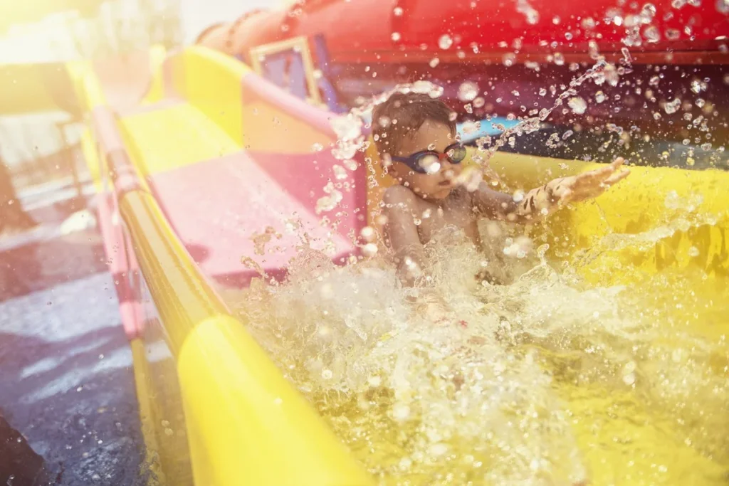 Niño con gafas de natación bajando por un tobogán amarillo en un parque acuático