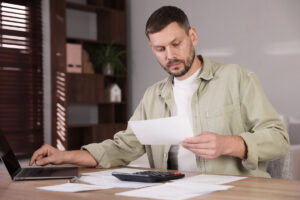 Hombre revisando documentos financieros en un escritorio con un portátil y una calculadora