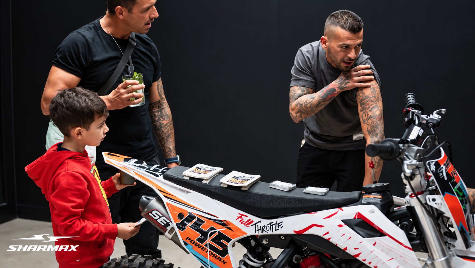 Dos adultos y un niño observan una pitbike blanca y naranja de Sharmax durante el evento.