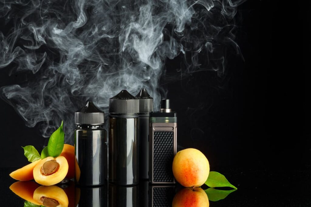 Vapeador tipo pod junto a botes de e-líquido con sabor a albaricoque y vapor blanco sobre fondo negro.